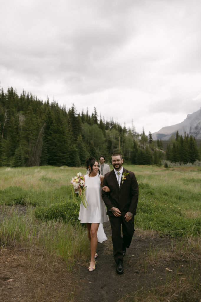 Bride and groom walking back down a dirt path as husband and wife after their intimate Banff National Park elopement ceremony at Mount Norquay Lookout.